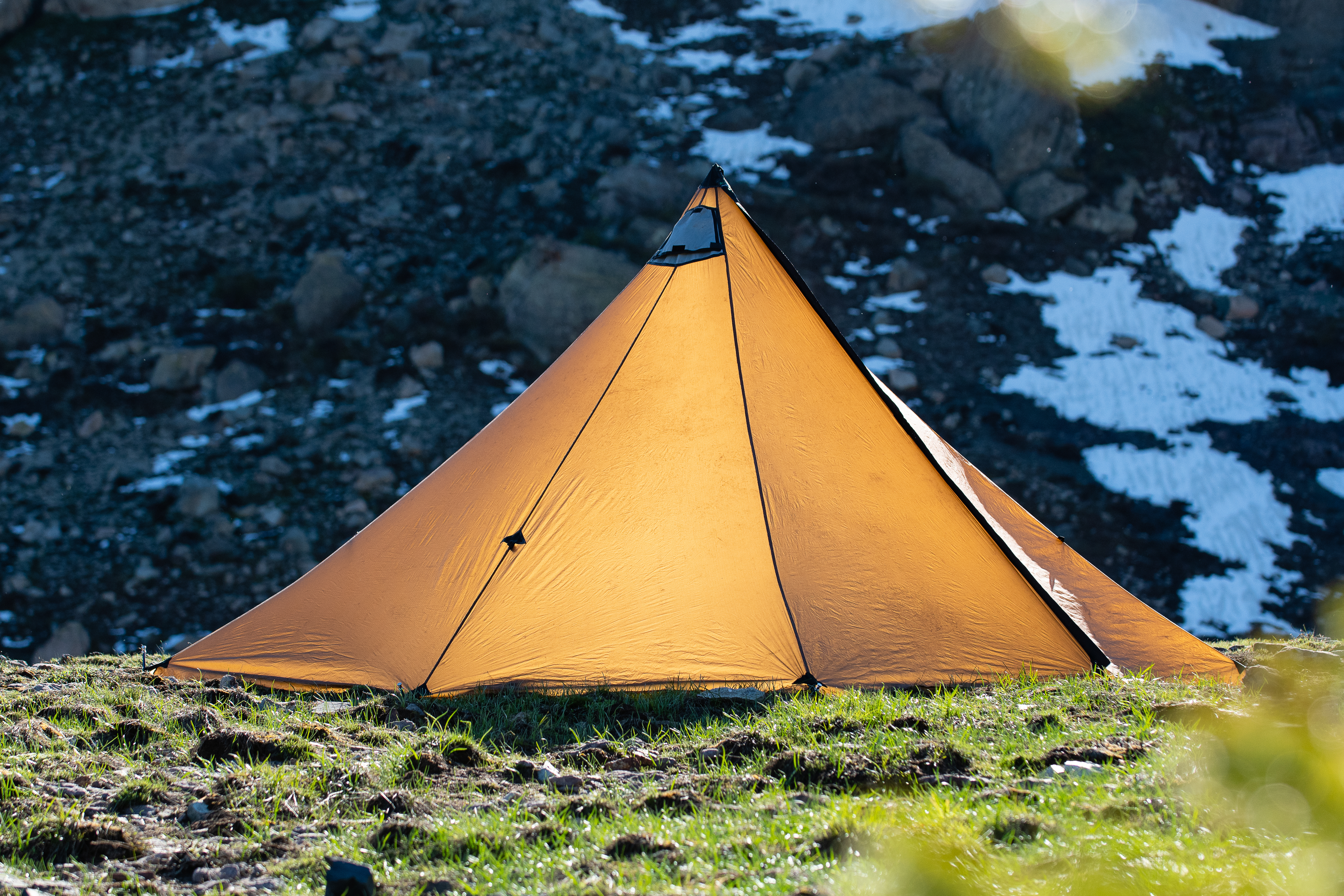 cimarron 2.0 in brown color with snow patches behing it in an alpine valley, the tent is quarterin away showing its multiple guy out points