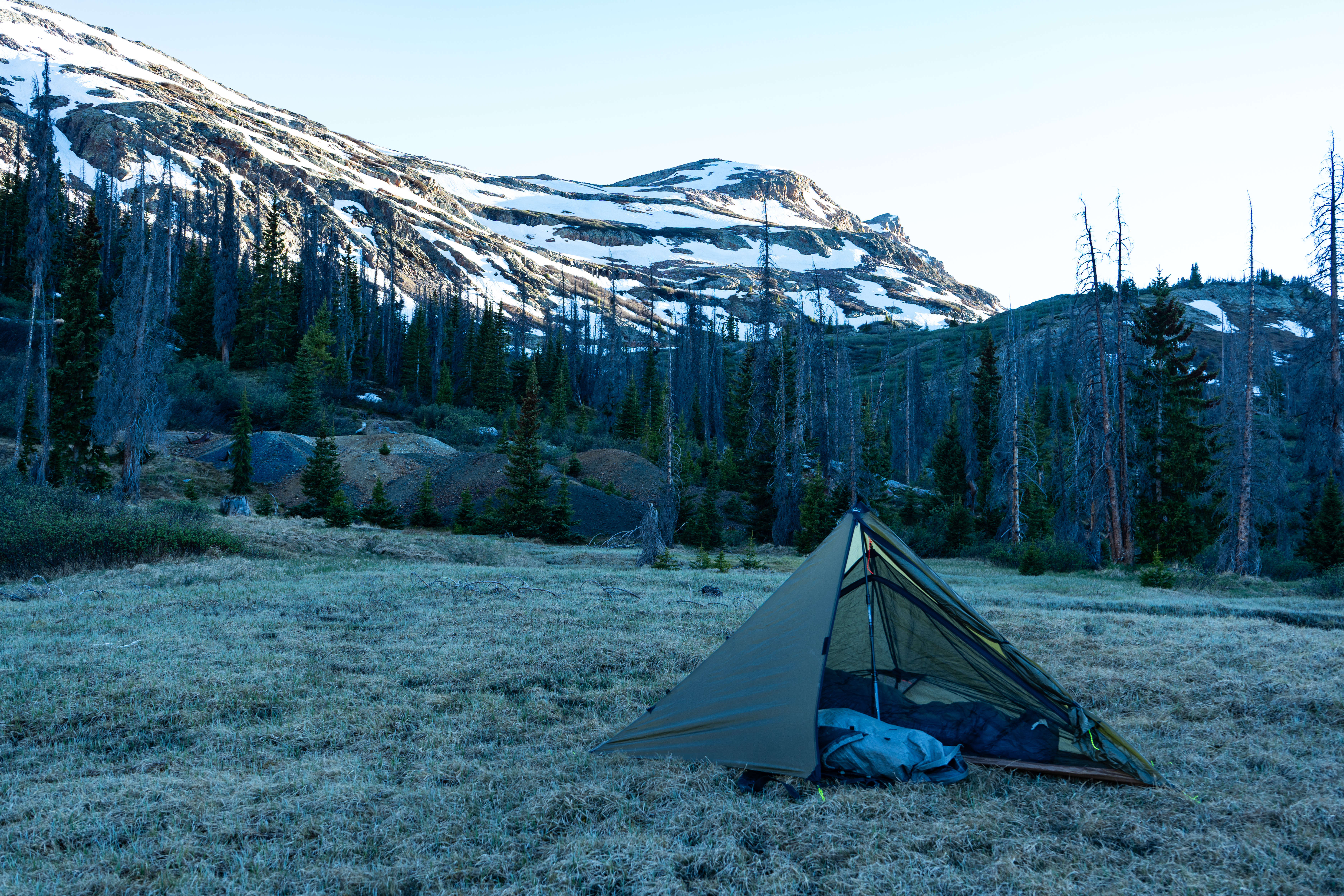 The Brightwater one person shelter in green color in an alpine valley sorrounded by snow capped mountains with the goshawk 6300 backpack in the vestibule